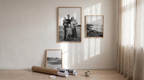 Natural oak picture frames with black and white photos in a sunlit room, one leaning by a shipping tube