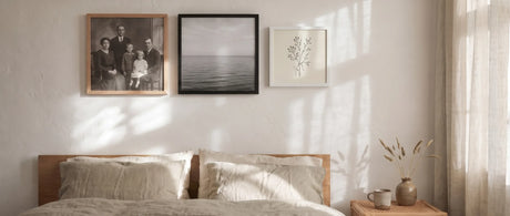 Square wood picture frames in oak, black and white above a linen bed in soft morning light