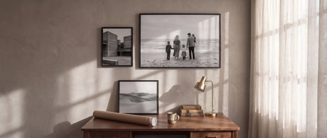 Black wood picture frames with black and white photos above a walnut desk in a sunlit study